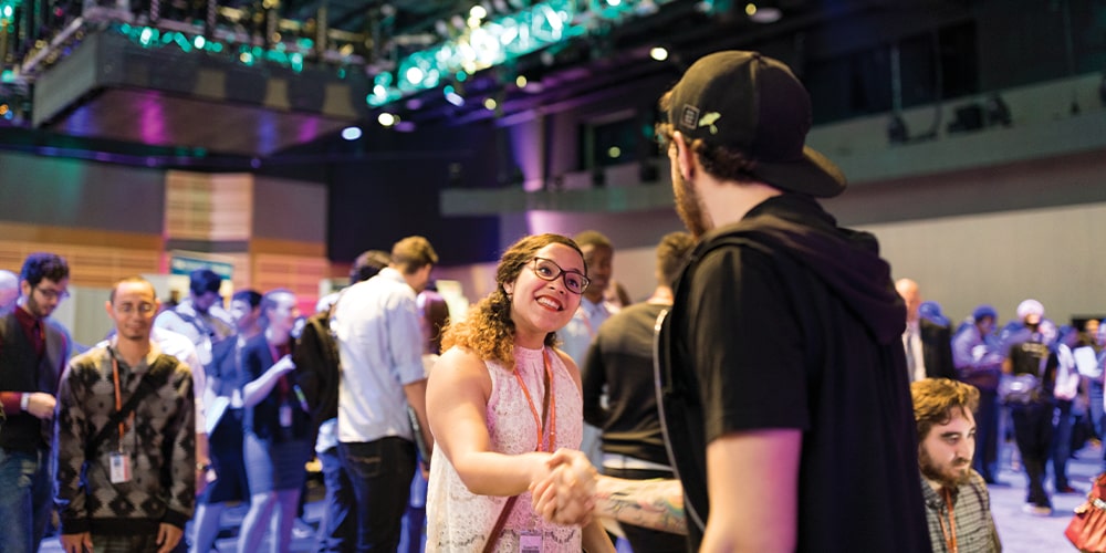 Woman shaking a man's hand in a room full of people.