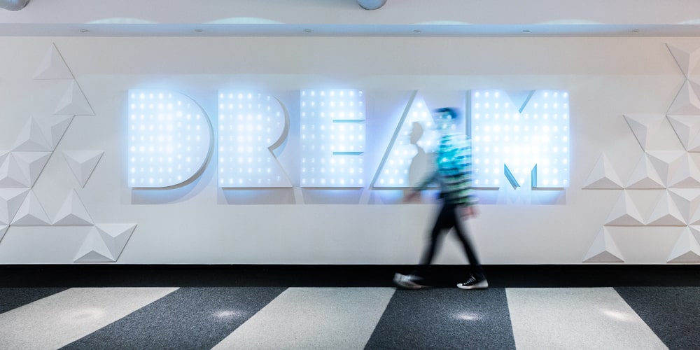 Male blurred with the word DREAM lit up on the wall behind him.