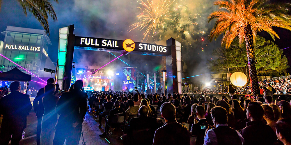 Nightime scene of Full Sail's campus, including a stage and fireworks, with many student and staff onlookers.