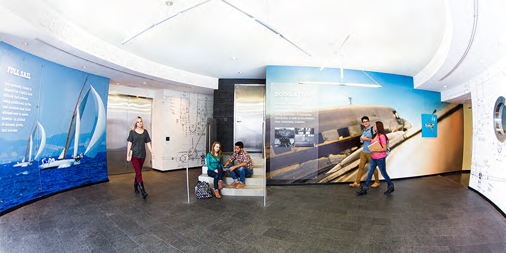 Various students sitting in and walking through a large hallway on Full Sail's campus.