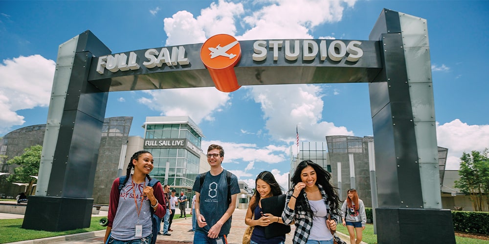 Five students walking underneath the Full Sail Studios archway at the front of campus.
